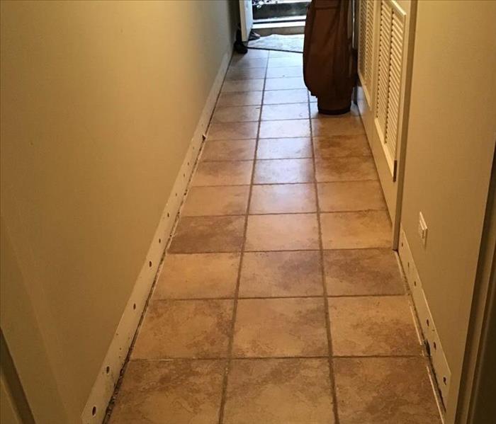 Dry brown tile in a hallway with the trim removed and a stairway in the background.