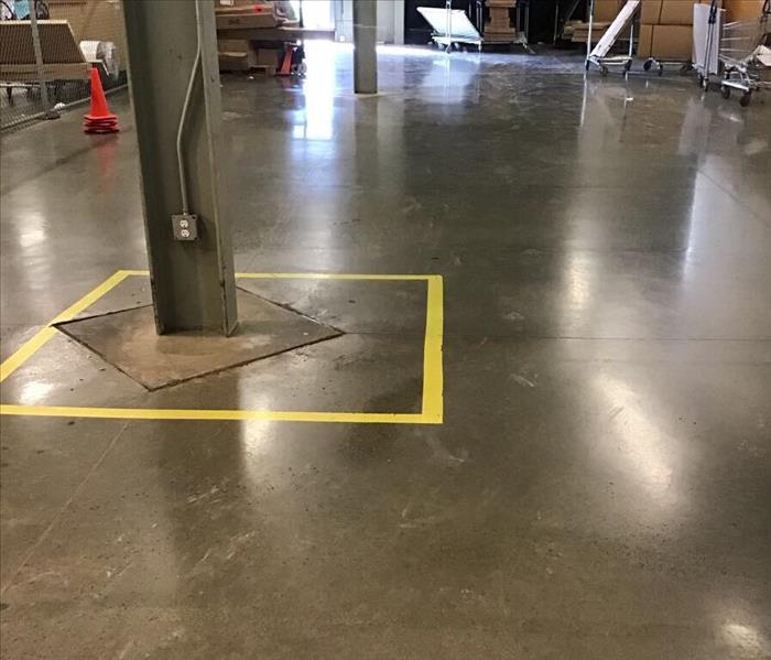 Dry concrete floor of a warehouse with a yellow square around a support beam in the background.