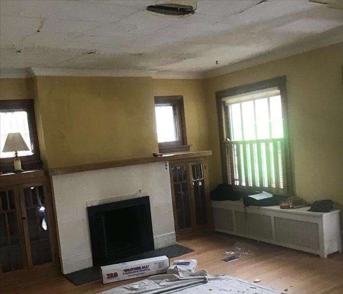 Dining room with a fireplace, yellow walls and a hole in the ceiling with debris on a tarp on the floor.