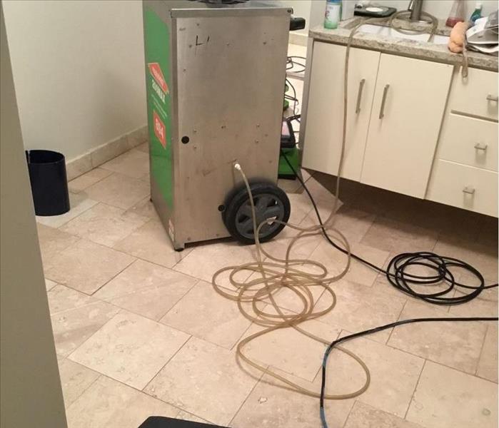 Clean light tan tile with a SERVPRO dehumidifier and a black air mover in a bathroom with white cabinets.