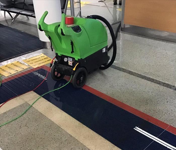 A green SERVPRO water extractor in a lobby of an office building with a wet floor.