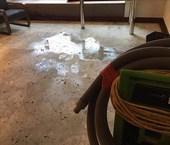 Wet concrete floor with a green SERVPRO extractor and a blue chair in the background.