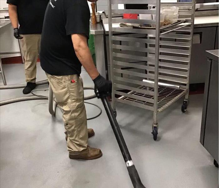 Two SERVPRO employees using a water extractor to clean a wet floor in a commercial kitchen.
