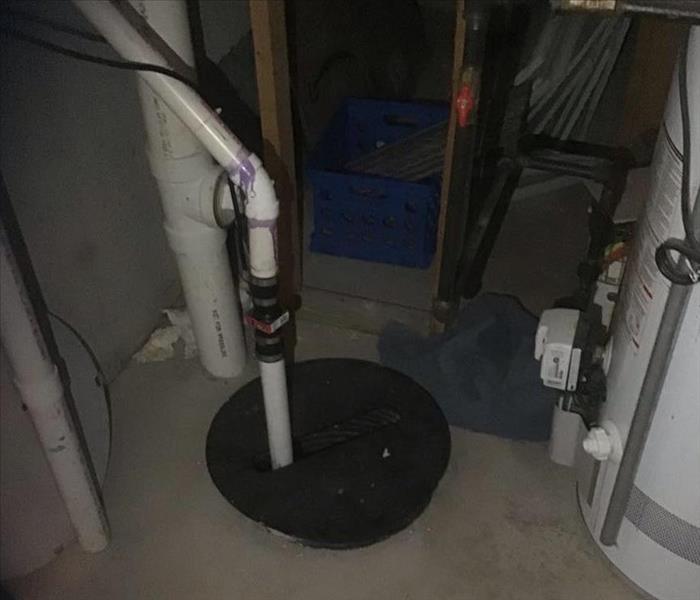 Basement floor with a sump pump and white plumbing pipes.