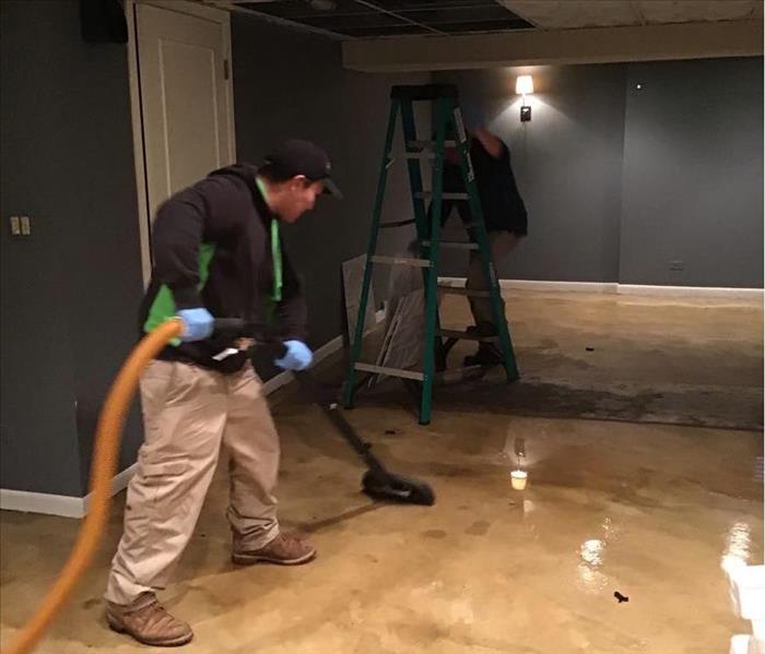 Wet concrete floor with a SERVPRO technician extracting water with equipment.