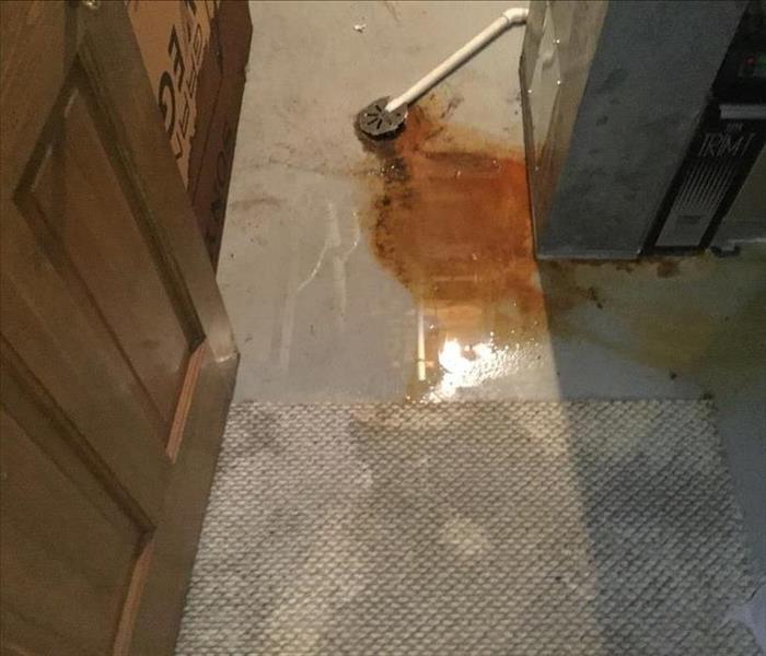 Wet brown carpet with rusty water on the floor in a furnace room.