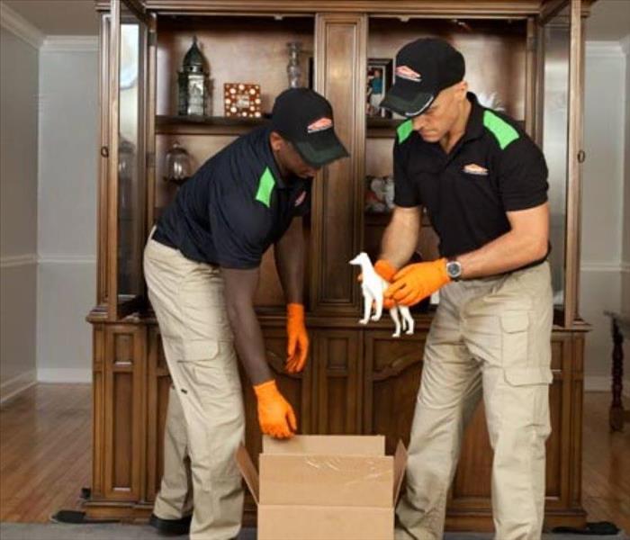 SERVPRO employees packing contents from a china cabinet in a living room.