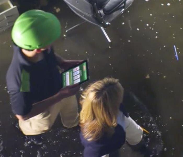 Flooded office with two people walking in the water holding an I-Pad looking at the damage.