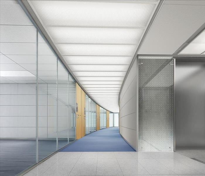Curved hallway of an office building with blue carpet, white tile and white lights in the ceiling.