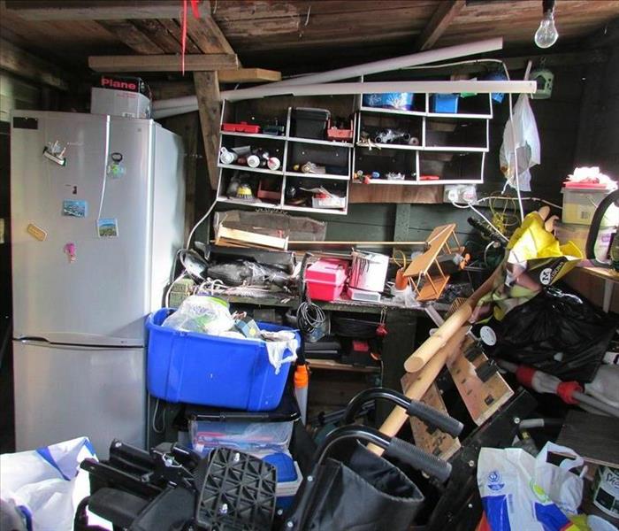Cluttered room with a white fridge and a blue bin in the background.