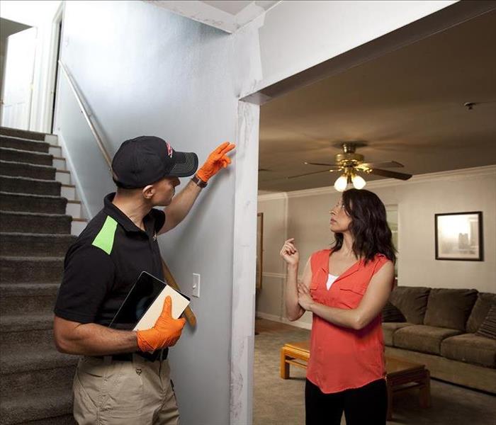 SERVPRO employee talking to a customer at the bottom of the stairs in the living room.