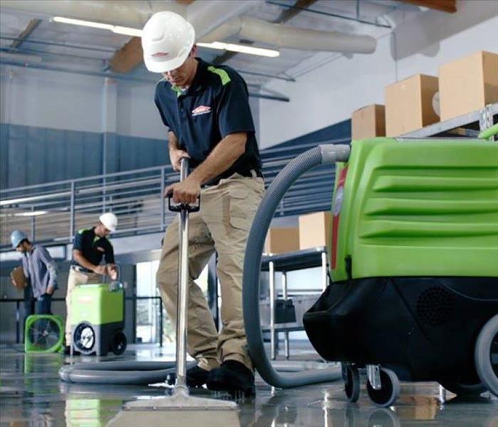SERVPRO employee using a green water extractor in a warehouse.